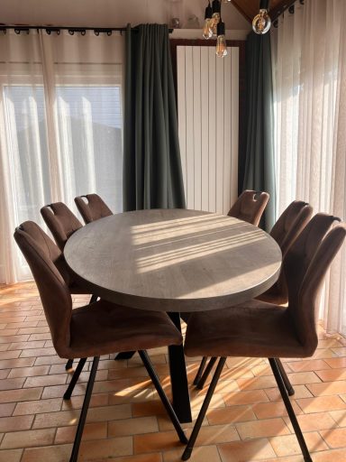 Eettafel Ronde tafel met zes stoelen, verlicht door natuurlijk licht door de ramen.