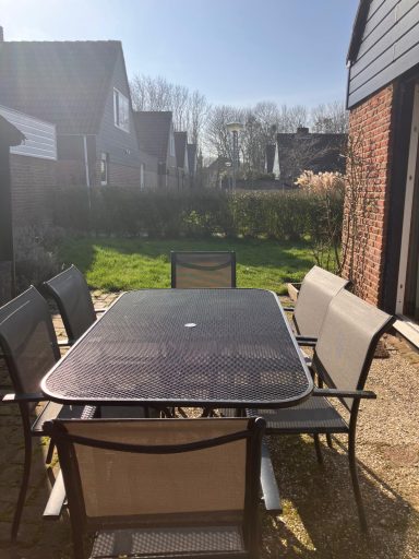 Tuin met tuintafel Tuintafel met stoelen in de zon, omringd door gras en huizen op de achtergrond.