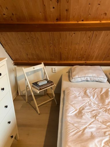 Slaapkamer Een kamer met een tweepersoonsbed, een opklapbare stoel en een kast tegen een houten wand.