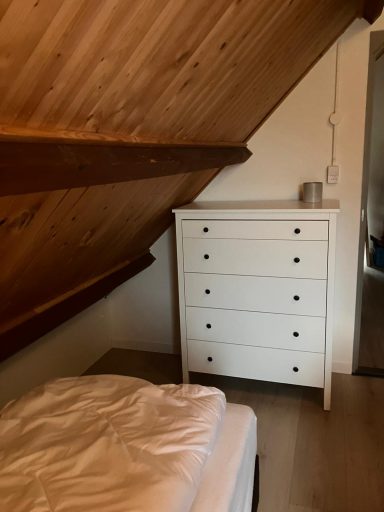 Slaapkamer Een slaapkamer met een schuin plafond, bed en witte ladekast.