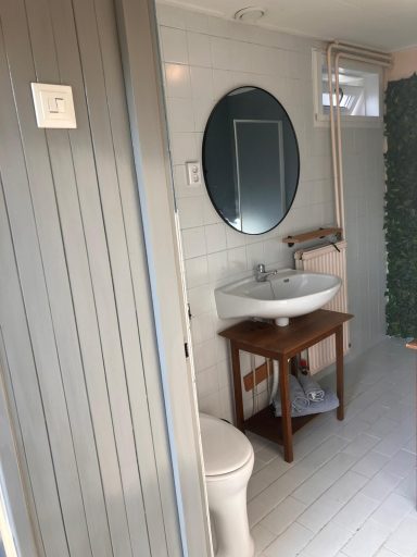 Badkamer Badkamer met wastafel, toilet en ronde spiegel, omringd door groene wand.