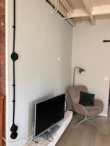 Woonkamer Woonkamer met een tv, een stijlvolle fauteuil en een lichtgrijze wand met buizen.